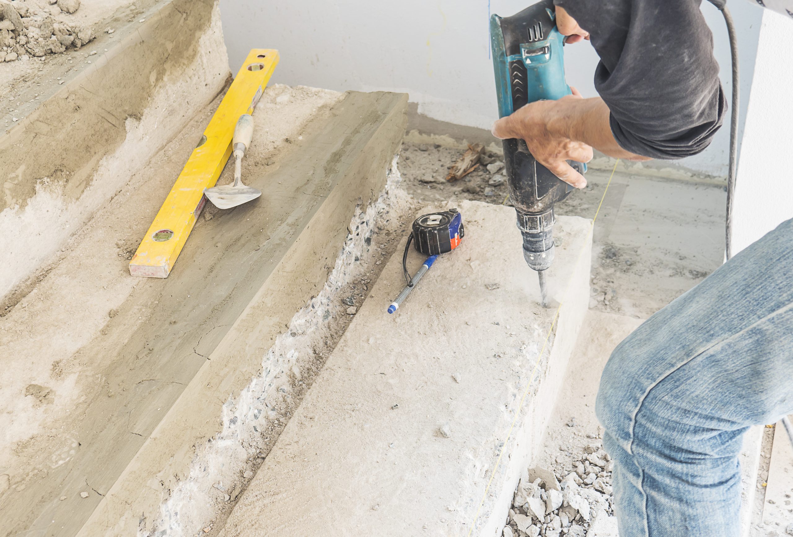 Partial focus of a man is working with reinforce concrete stair structure modification using hand drill machine in construction site